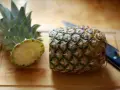 En ananas är delad på mitten på en skärbräda, redo för att visa hur skalar man en ananas. En kniv ligger bredvid.