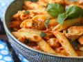 En skål med penne pasta med kyckling i en kryddig tomatsås med sambal oelek, toppad med färsk basilika.