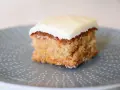 En bit saftig glutenfri morotskaka med krämig glasyr på en gråblå tallrik med prickigt mönster.