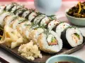 Välsmakande hemmagjord sushi med lax, gurka och krämig fyllning, garnerad med dill och sesamfrön. Serveras med ingefära och wasabi.