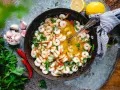 En panna med saftiga räkor i en gyllene sås, perfekt för ett snabbt gambas recept. Garnerad med färsk persilja, chili och vitlök.