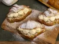 Tre semlor fyllda med grädde och mandelmassa, pudrade med florsocker på en träbricka.