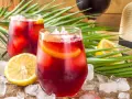 Två glas med tinto de verano, is och citronskivor, omgivna av palmblad och en sommarhatt. Perfekt för en varm dag.