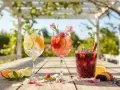 Tre färgglada sangrior med frukt och mynta på ett träbord utomhus. Perfekt för ett enkelt sangria recept.
