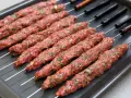 Råa adana kebab-spett med lök och persilja på en plåt, redo för grillen.