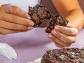 Händerna bryter isär en saftig chokladkaka, strödd med flingsalt. En hel kaka ligger på en tallrik.