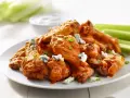 En tallrik med saftiga buffalo wings, toppade med blåmögelost och gräslök, serveras med selleristavar och en skål med dippsås.