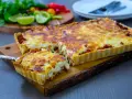 En gyllene tacopaj med en krämig fyllning och köttfärs, redo att serveras. Tillbehören med lime och koriander antyder ett smakrikt tacopaj recept.