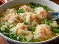 En skål med ångande dumplings i buljong, garnerad med färska örter och salladslök. En perfekt och värmande måltid.
