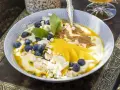 En skål med yoghurt, blåbär, passionsfrukt och vackert skivad mango. Toppad med kokoschips och puffat spannmål.