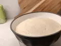 En fluffig pizzadeg i en skål, redo att frysa in för framtida pizzakvällar. En mjölpåse syns i bakgrunden.