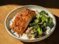 En skål med ris, saftig lax teriyaki toppad med sesamfrön och ångad broccoli.