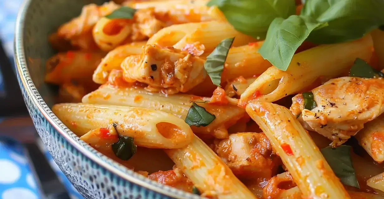 En skål med penne pasta med kyckling i en kryddig tomatsås med sambal oelek, toppad med färsk basilika.