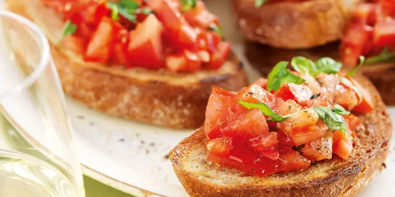 Krispiga bruschettor med färska tomater och basilika, perfekt för ett italienskt recept. Ett glas vitt vin till.