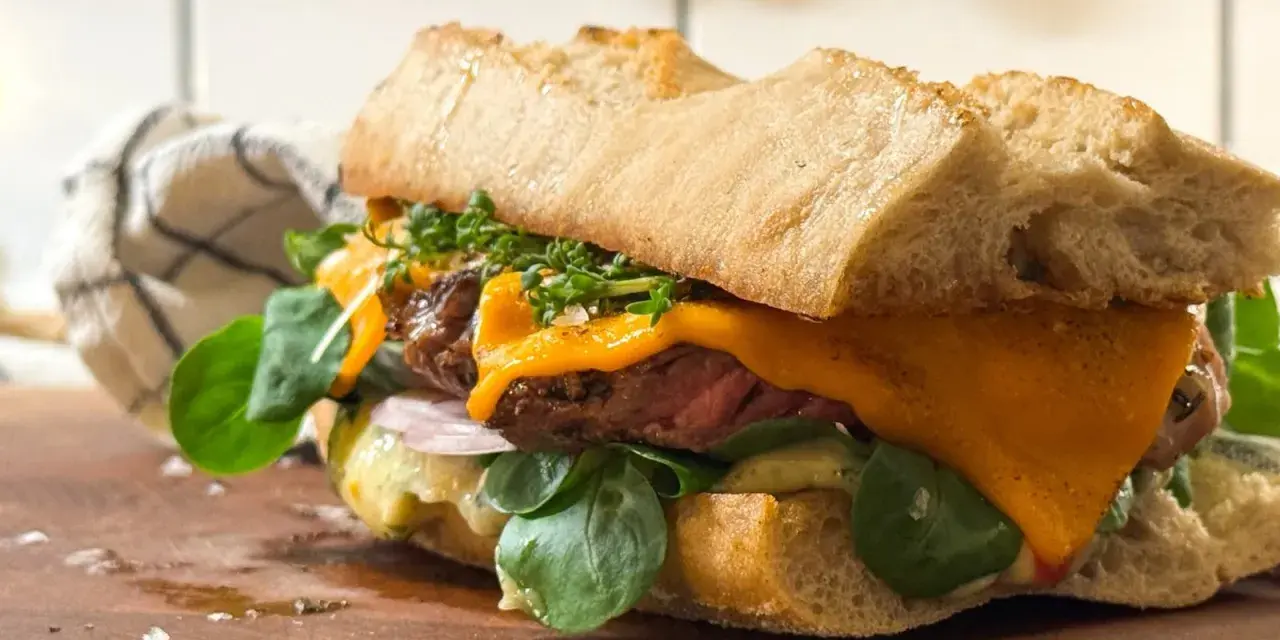 En saftig steak sandwich med smält ost, färska gröna blad och krispigt bröd.