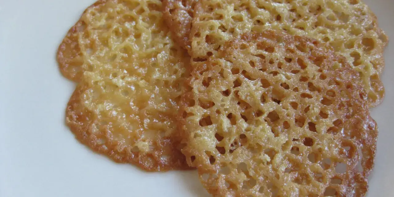 Tre gyllene, tunna havreflarn med ett vackert nätmönster ligger på en vit tallrik. Perfekt för ett enkelt havreflarn recept.