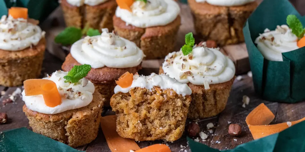 Fluffiga morotskaka muffins med krämig frosting, toppade med nötter och en liten morotsdekoration. Perfekta för fikat!