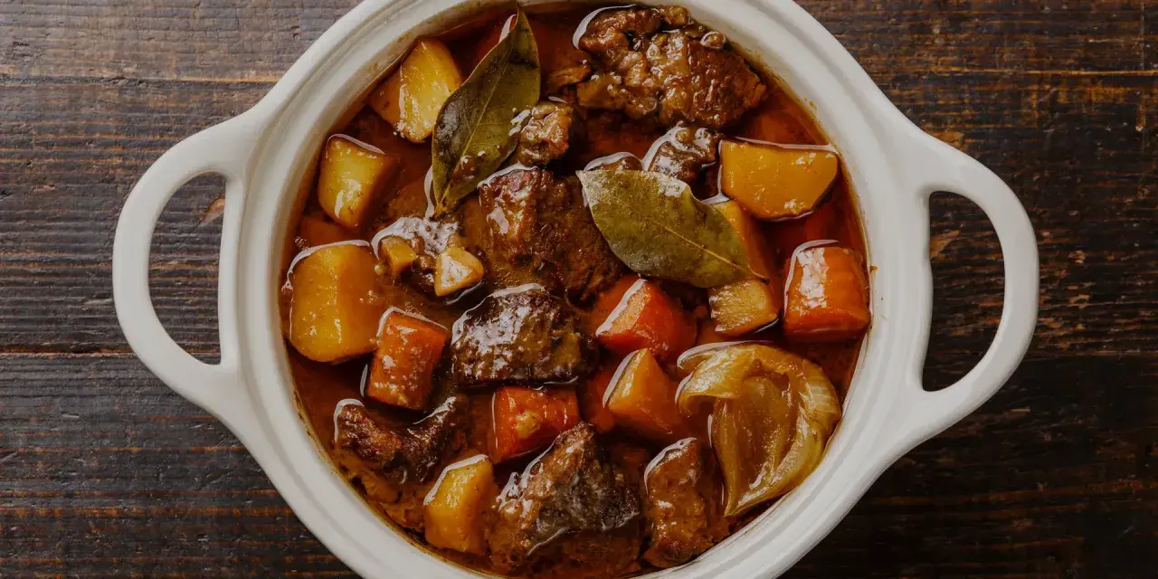 En vit gryta fylld med mustig boeuf bourguignon, med möra köttbitar, potatis och morötter. Perfekt vin till boeuf bourguignon.