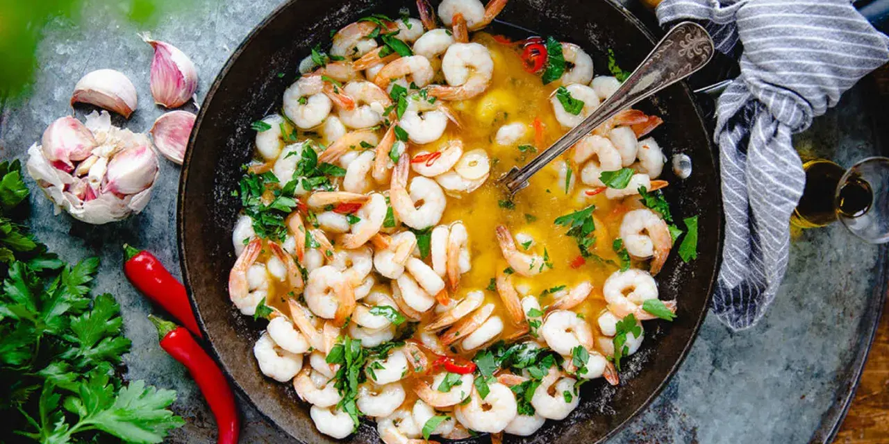 En panna med saftiga räkor i en gyllene sås, perfekt för ett snabbt gambas recept. Garnerad med färsk persilja, chili och vitlök.