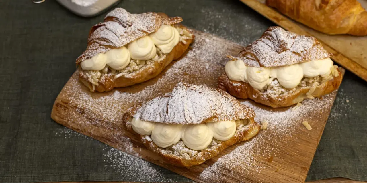 Tre semlor fyllda med grädde och mandelmassa, pudrade med florsocker på en träbricka.