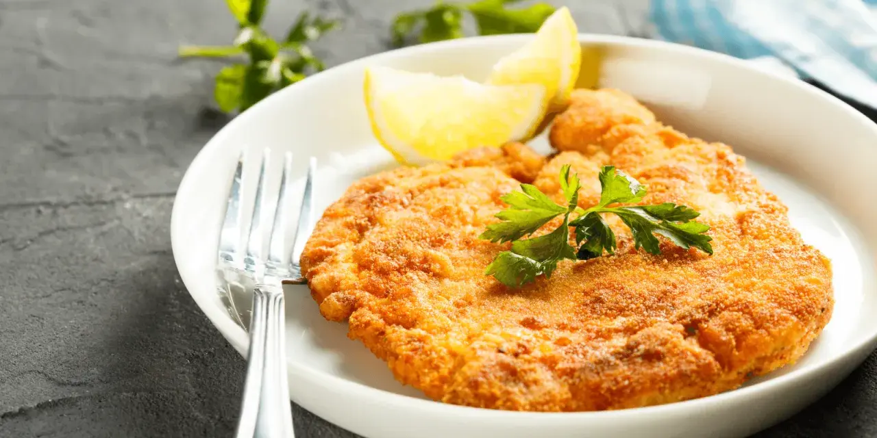 En gyllene schnitzel med citron och persilja, perfekt till ett glas vin.