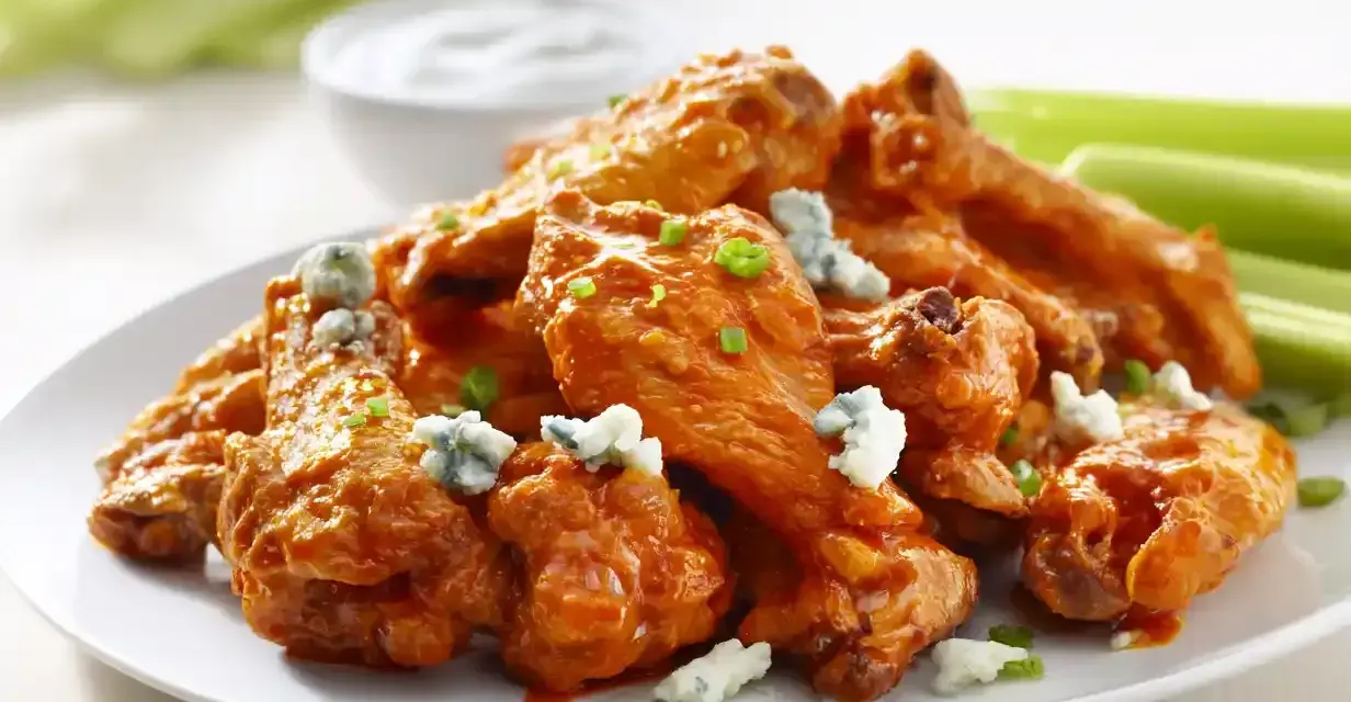En tallrik med saftiga buffalo wings, toppade med blåmögelost och gräslök, serveras med selleristavar och en skål med dippsås.