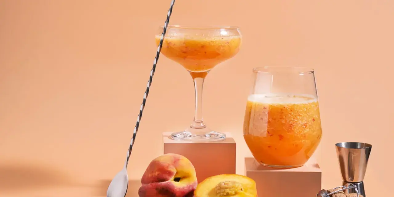 Två glas med persikojuoma, persikor och en barsked. Ett enkelt bellini recept för en solig dag.