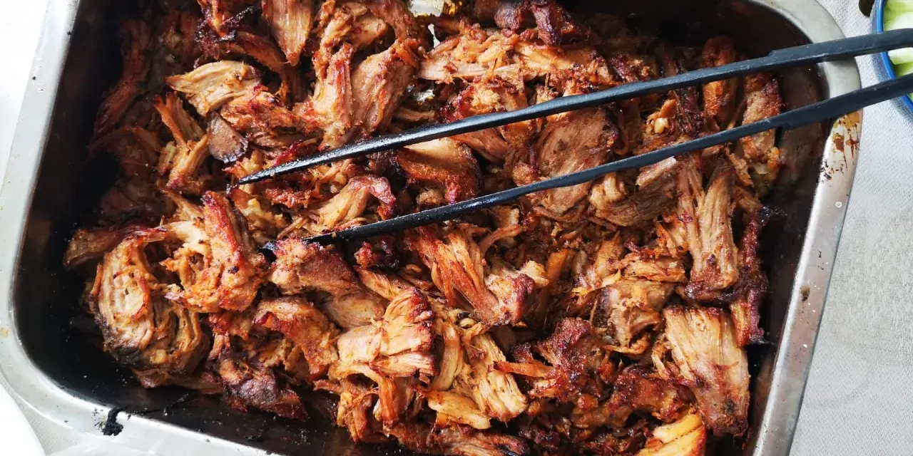 Saftigt, dras isär fläskkött i en ugnsform, redo att serveras. Ett perfekt carnitas recept för en festmåltid.