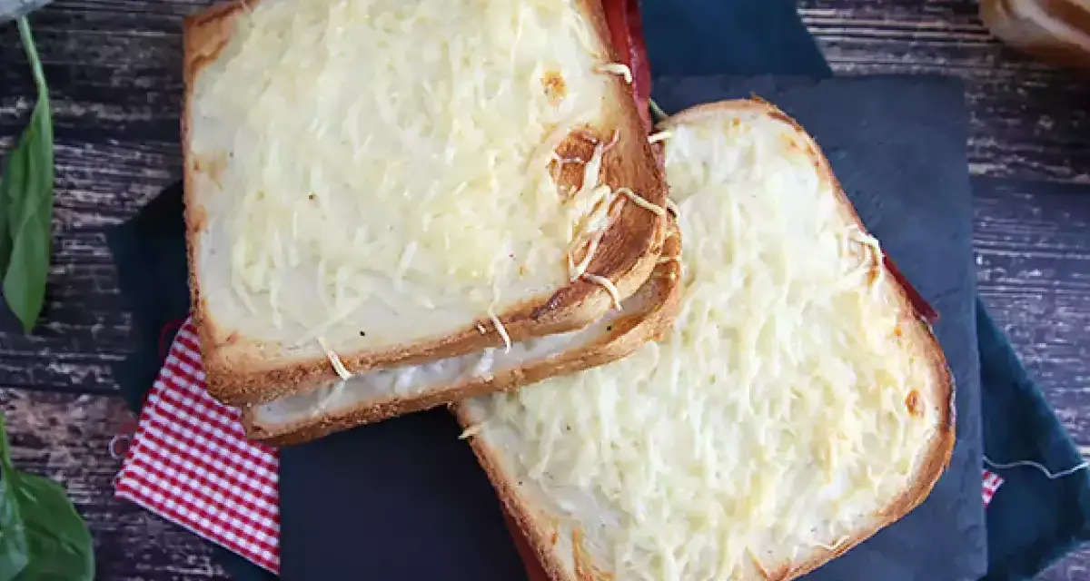 Två gyllene croque monsieur-smörgåsar med smält ost och skinka, serverade på en rutig duk.