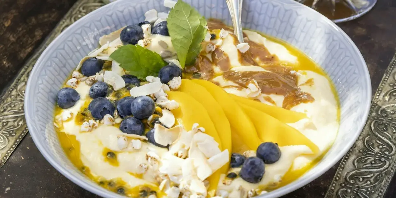 En skål med yoghurt, blåbär, passionsfrukt och vackert skivad mango. Toppad med kokoschips och puffat spannmål.