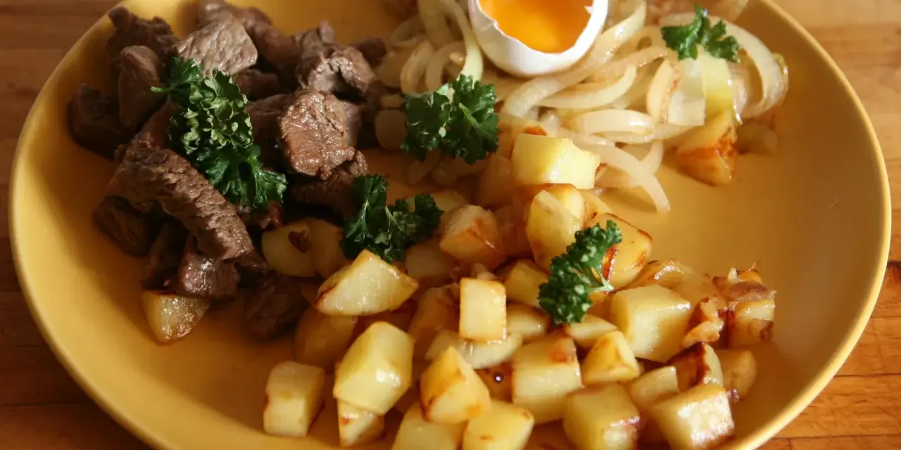 En tallrik med stekt kött, stekt potatis, stekt lök och ett kokt ägg. Ett klassiskt husmanskost recept som passar perfekt för en vardagsmiddag.