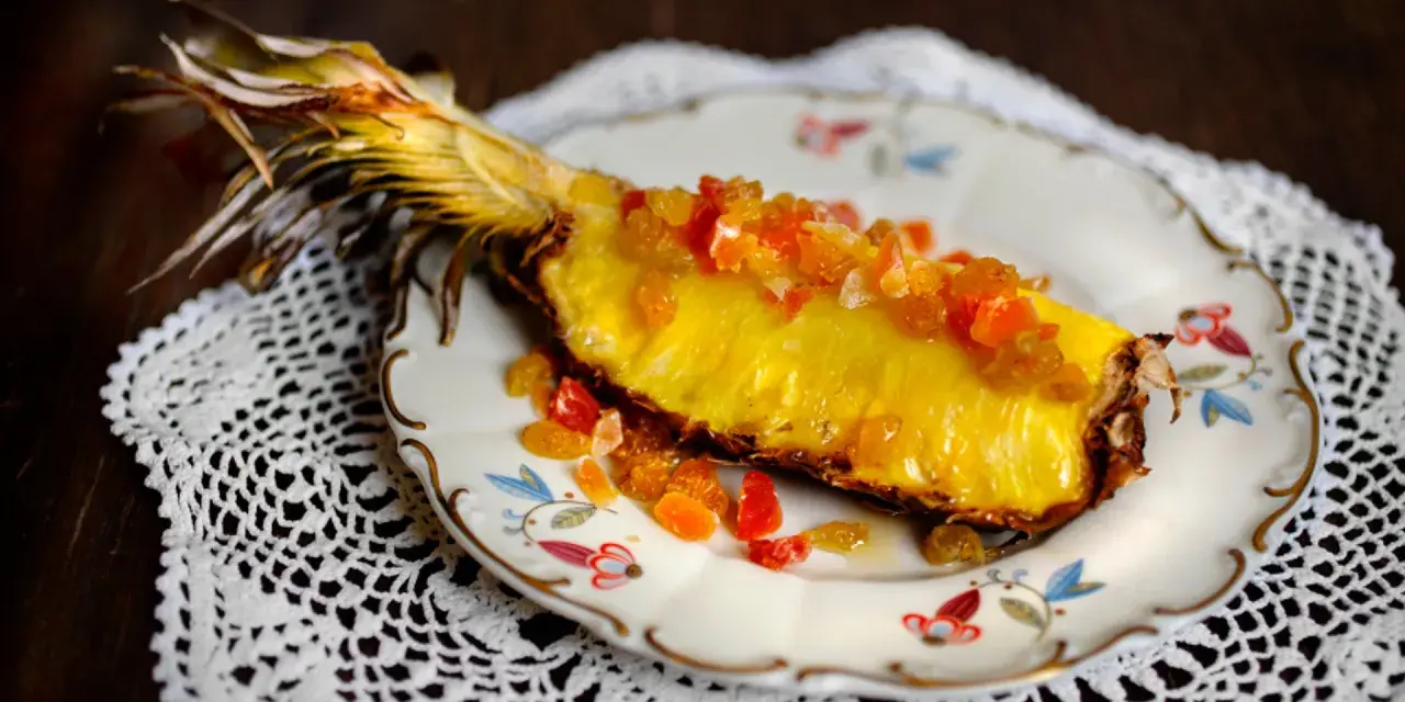 En saftig ananasskiva, toppad med kanderad frukt, serverad på en vacker tallrik. Ett konstverk som visar hur man kan dela ananas utan kniv.