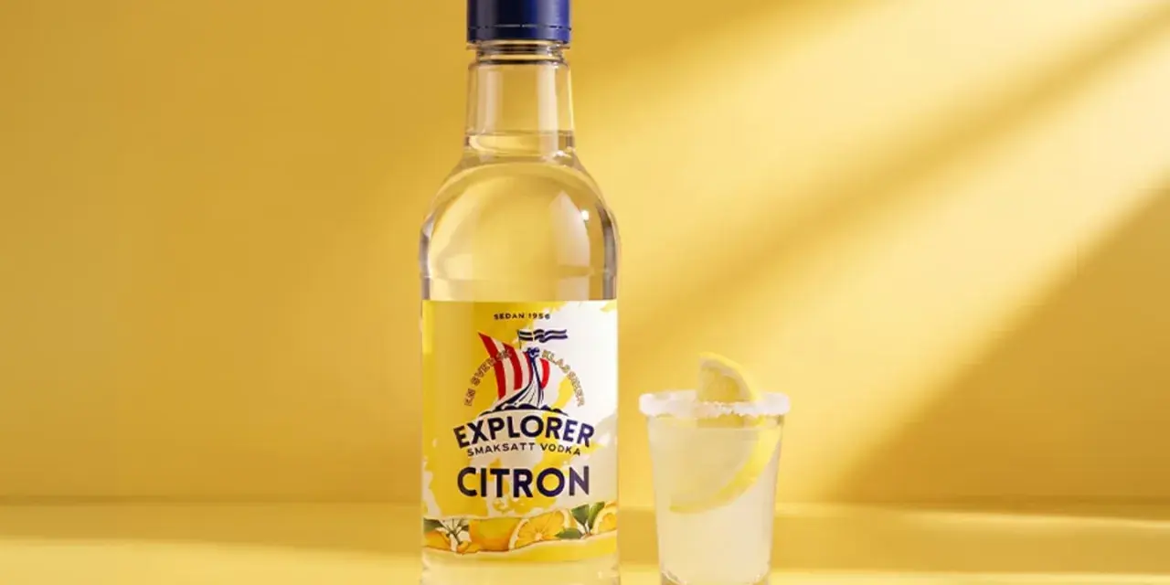 En flaska Explorer Citron vodka bredvid ett glas med en lemon drops shot, garnerad med citronskiva och saltkant.