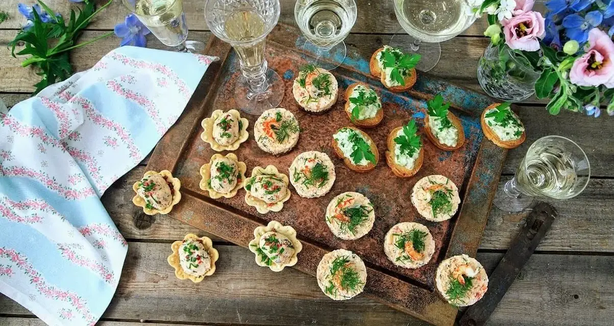 Små, läckra snacks till bubbel, serverade på ett fat med blommor och glas. Perfekt för en festlig stund.