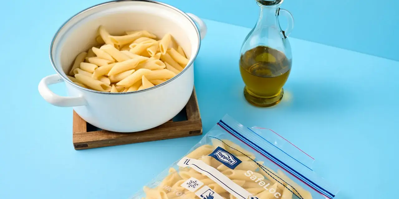 Koka pasta och förbered för att frysa in den. En kastrull med penne, en flaska olivolja och en fryspåse syns.