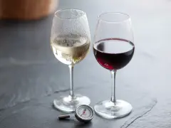 Två glas vin, ett vitt och ett rött, med en termometer bredvid. Perfekt vitt vin temperatur är viktigt för njutning.