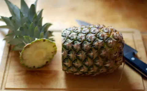 En ananas är delad på mitten på en skärbräda, redo för att visa hur skalar man en ananas. En kniv ligger bredvid.