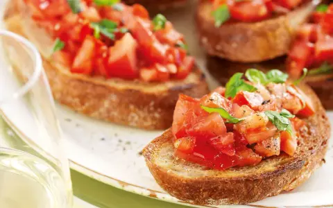 Krispiga bruschettor med färska tomater och basilika, perfekt för ett italienskt recept. Ett glas vitt vin till.