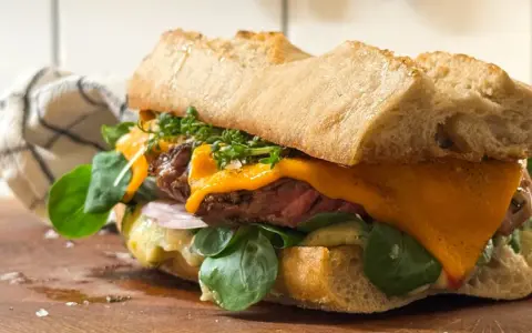 En saftig steak sandwich med smält ost, färska gröna blad och krispigt bröd.