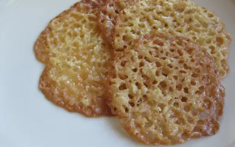 Tre gyllene, tunna havreflarn med ett vackert nätmönster ligger på en vit tallrik. Perfekt för ett enkelt havreflarn recept.