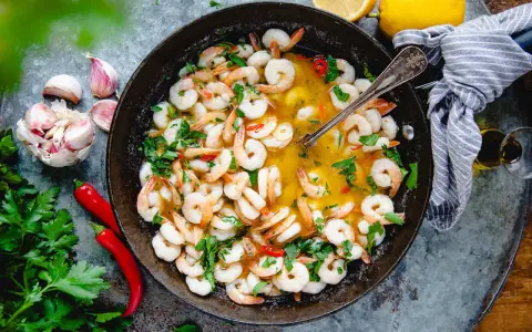 En panna med saftiga räkor i en gyllene sås, perfekt för ett snabbt gambas recept. Garnerad med färsk persilja, chili och vitlök.