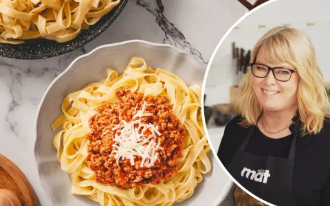 En kvinna med glasögon ler bredvid en skål med tagliatelle och köttfärssås. Perfekt för en snabb middag, den kokta pastan i kylen är redo att serveras.