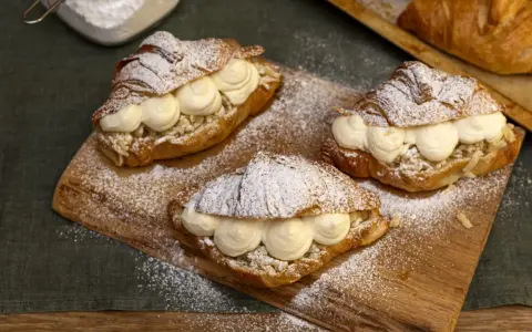 Tre semlor fyllda med grädde och mandelmassa, pudrade med florsocker på en träbricka.
