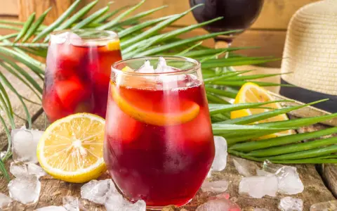 Två glas med tinto de verano, is och citronskivor, omgivna av palmblad och en sommarhatt. Perfekt för en varm dag.