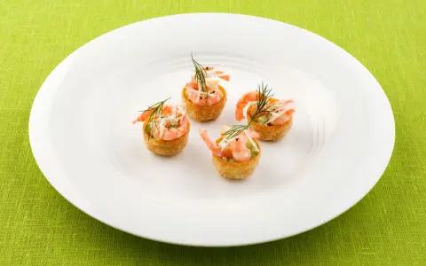 Fyra små, krispiga tempura rolls med räkor och dill på en vit tallrik.