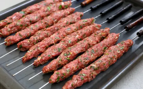 Råa adana kebab-spett med lök och persilja på en plåt, redo för grillen.