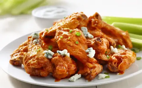 En tallrik med saftiga buffalo wings, toppade med blåmögelost och gräslök, serveras med selleristavar och en skål med dippsås.