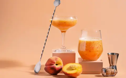 Två glas med persikojuoma, persikor och en barsked. Ett enkelt bellini recept för en solig dag.