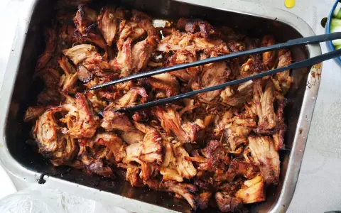 Saftigt, dras isär fläskkött i en ugnsform, redo att serveras. Ett perfekt carnitas recept för en festmåltid.