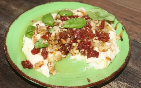 Vispad brie med soltorkade tomater, valnötter och färsk basilika på en grön tallrik. En läcker förrätt som passar perfekt till vin.